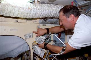 Mission specialist Vladimir Titov points to a dollar bill which has been taped to the Base Block wall.